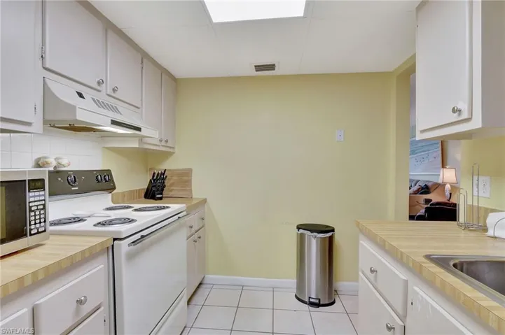 Kitchen featuring decorative backsplash, white cabinets, electric stove, and light tile patterned floors