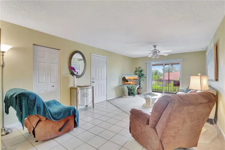 Living room with a textured ceiling, light tile patterned floors, and ceiling fan
