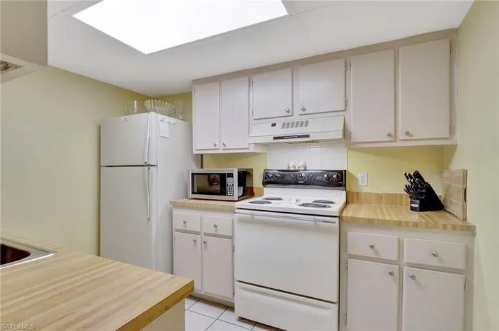Kitchen featuring white cabinetry, white appliances, light tile patterned floors, premium range hood, and decorative backsplash