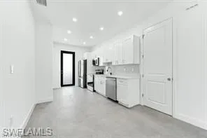 Kitchen #1 featuring stainless steel dishwasher, white cabinetry, light countertops, recessed lighting, and concrete flooring