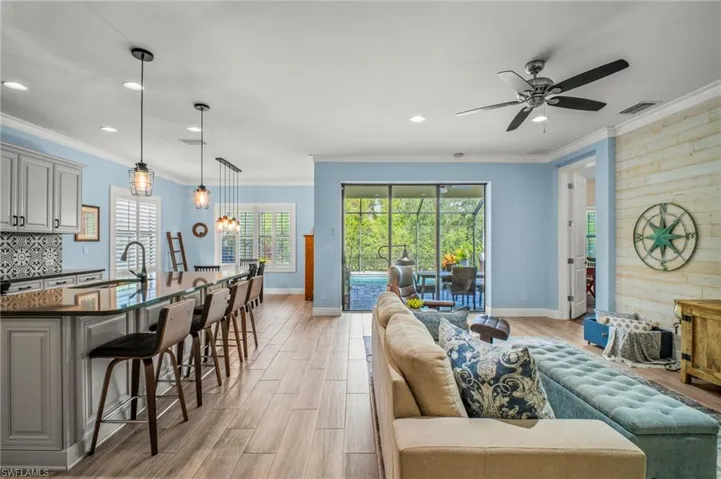 Living area with wood tiled floors, plenty of natural light, suspended lighting, ceiling fan, and crown molding