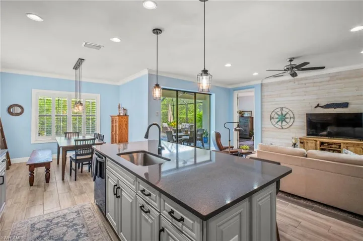 Kitchen with open floor plan, wood tiled floors, a kitchen island with sink, pendant lighting, and dark stone counters