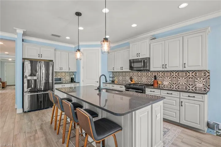 Kitchen featuring a kitchen bar, stainless steel appliances, an island with sink, light wood-style floors, and white cabinetry