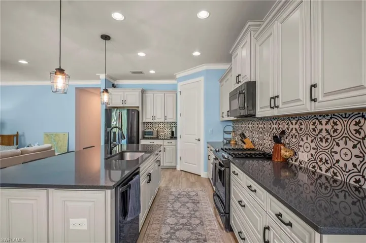 Kitchen with stainless steel appliances, dark stone countertops, light wood-type flooring, a center island with sink, and hanging light fixtures