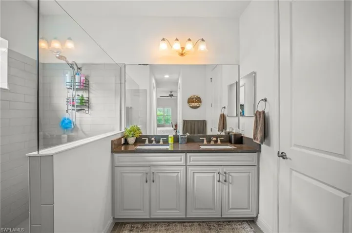 Bathroom featuring double vanity, walk in shower, and a ceiling fan