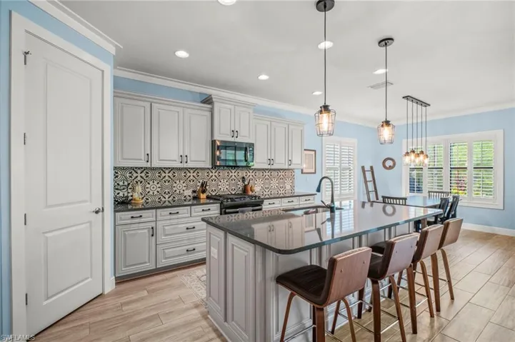 Kitchen featuring wood finish floors, a kitchen breakfast bar, backsplash, stainless steel microwave, and ornamental molding