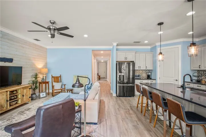 Living area with light wood-type flooring, wooden walls, ceiling fan, crown molding, and recessed lighting