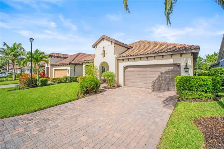 Mediterranean / spanish home featuring stucco siding, decorative driveway, a garage, a front lawn, and a tiled roof