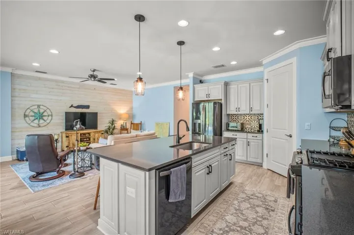 Kitchen with stainless steel appliances, open floor plan, light wood-style floors, a kitchen island with sink, and crown molding