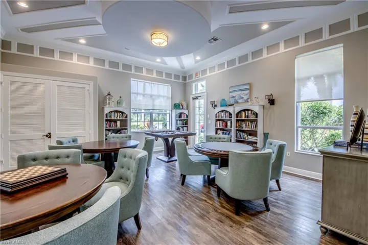 Sophisticated home office featuring coffered ceiling with recessed lighting, built-in shelving throughout, wood-finish flooring, and multiple large windows with natural light