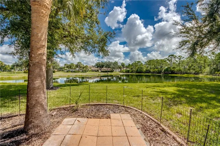Expansive grassy area with a reflective pond, mature trees, and a paver patio
