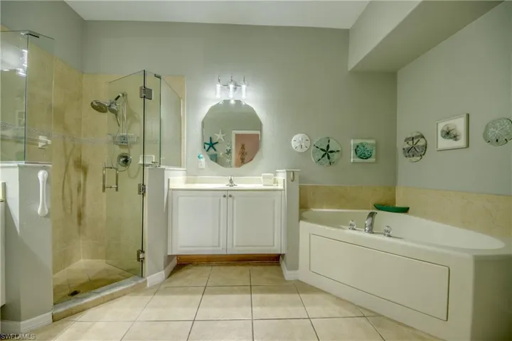 Glass-enclosed shower with tiled surround, separate soaking tub, single vanity with white cabinetry, polished chrome fixtures, and tiled flooring