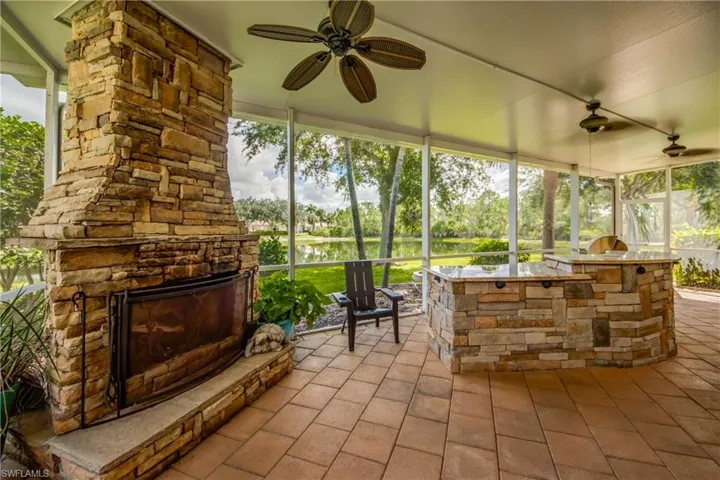 Screened patio featuring a stacked stone fireplace, stone-clad outdoor kitchen, paver flooring, and ceiling fans