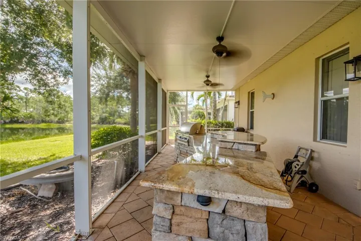Screened outdoor living area featuring a built-in outdoor kitchen with grill, stone base, and stone countertops