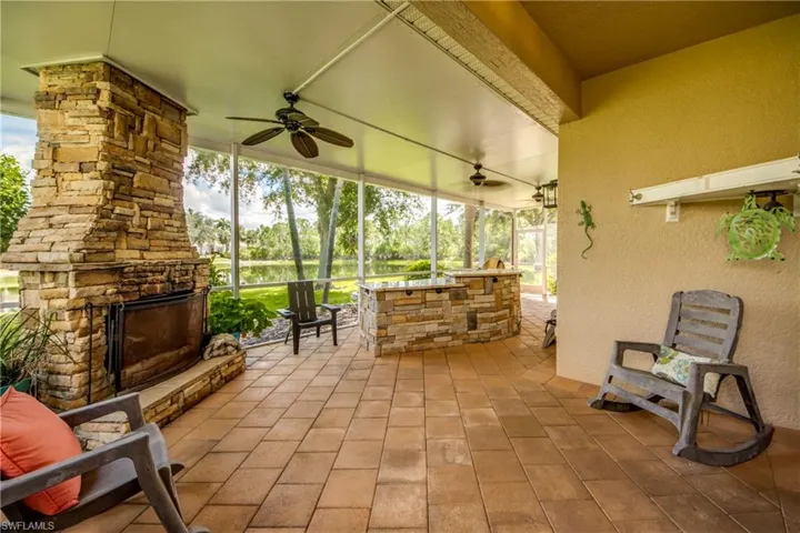 Screened lanai featuring a stone-clad fireplace and an outdoor kitchen with stone veneer