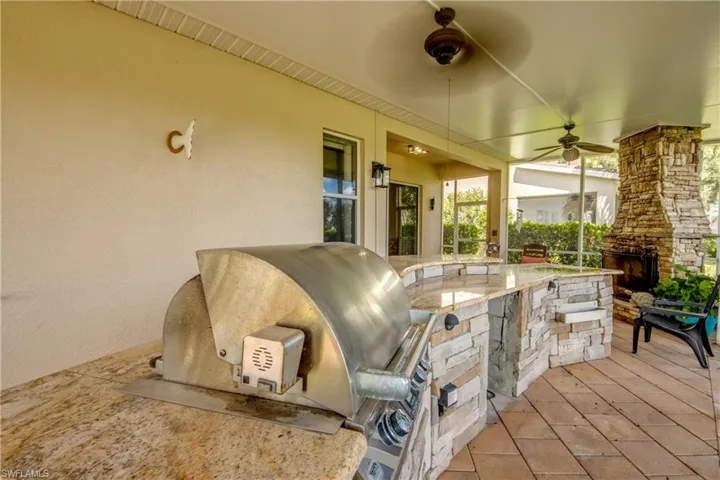 Outdoor kitchen with built-in stainless steel grill, stone-clad island, and granite countertops