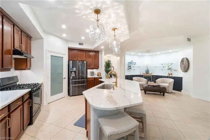 Kitchen with hanging light fixtures, sink, a center island with sink, stainless steel fridge with ice dispenser, and gas stove