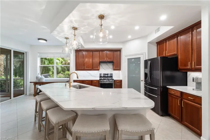 Kitchen featuring pendant lighting, a chandelier, an island with sink, decorative backsplash, and appliances with stainless steel finishes