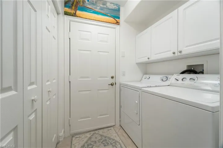Clothes washing area featuring cabinets, light tile patterned flooring, and washing machine and dryer