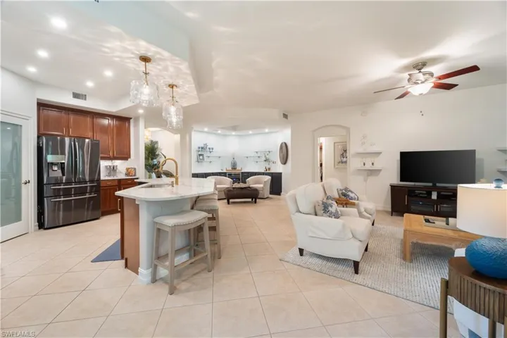 Kitchen with hanging light fixtures, light tile patterned floors, ceiling fan with notable chandelier, and stainless steel fridge with ice dispenser