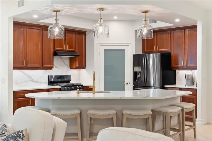Kitchen featuring light stone countertops, black gas range, decorative light fixtures, stainless steel refrigerator with ice dispenser, and sink