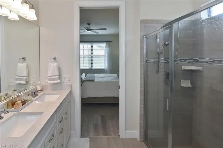 Bathroom featuring double vanity, ensuite bathroom, a shower stall, light wood finished floors, and ceiling fan