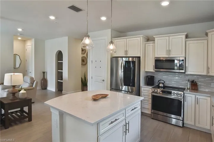 Kitchen with stainless steel appliances, decorative backsplash, a center island, pendant lighting, and light stone counters
