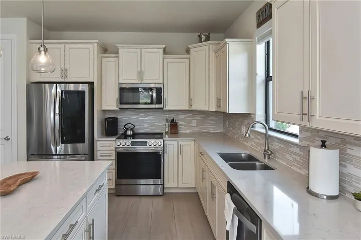 Kitchen featuring appliances with stainless steel finishes, backsplash, light stone counters, and decorative light fixtures