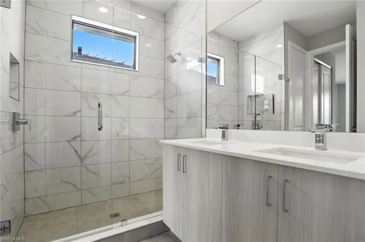 Bathroom with a marble finish shower, healthy amount of natural light, and double vanity