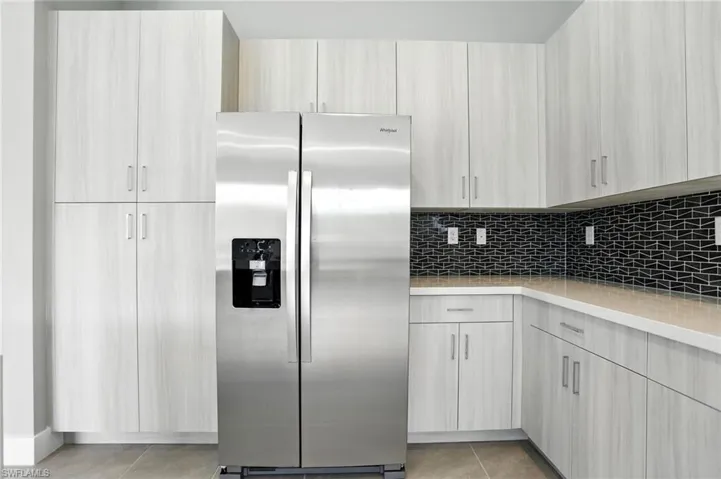 Kitchen with stainless steel fridge with ice dispenser, tasteful backsplash, light tile patterned floors, modern cabinets, and light stone counters