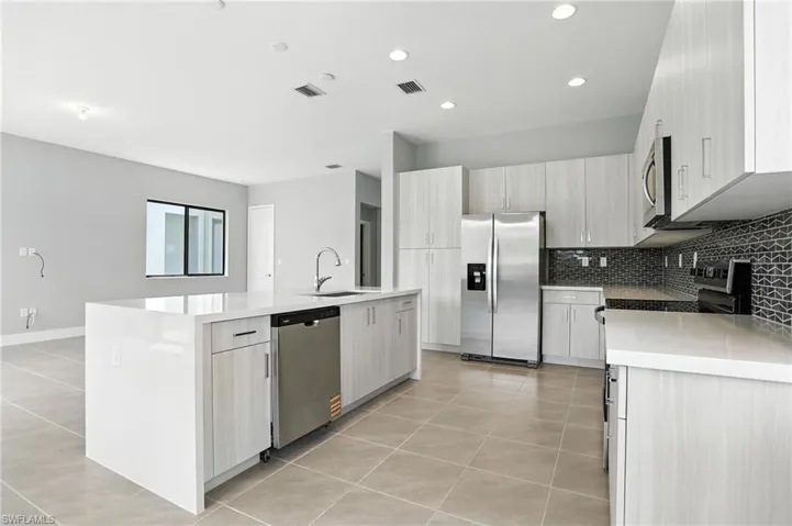 Kitchen with light tile patterned flooring, stainless steel appliances, decorative backsplash, light stone countertops, and recessed lighting