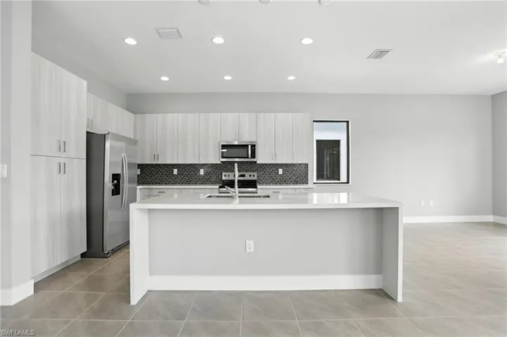 Kitchen with appliances with stainless steel finishes, tasteful backsplash, modern cabinets, light tile patterned floors, and light stone countertops
