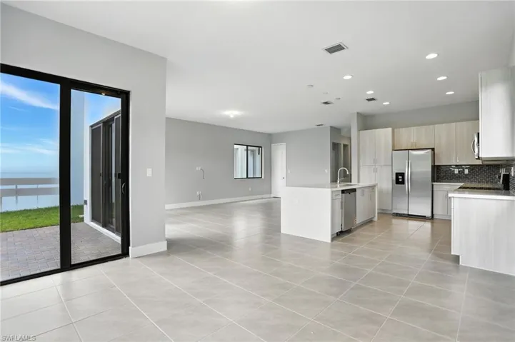 Kitchen featuring appliances with stainless steel finishes, light tile patterned floors, backsplash, open floor plan, and an island with sink
