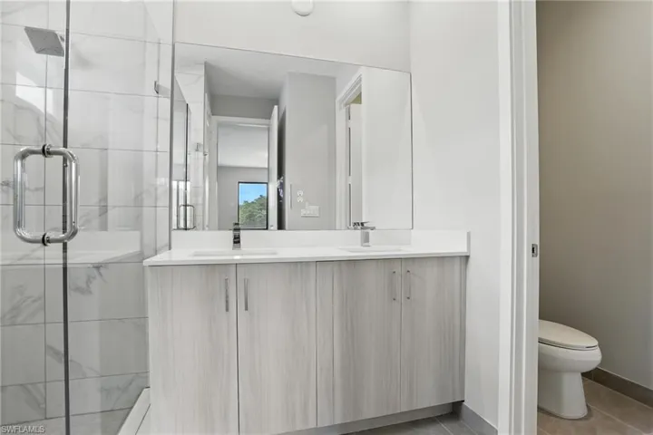 Bathroom featuring a marble finish shower, double vanity, and tile patterned flooring
