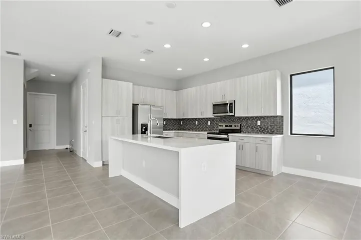 Kitchen with stainless steel appliances, light tile patterned flooring, a center island with sink, decorative backsplash, and recessed lighting