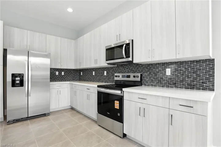 Kitchen with appliances with stainless steel finishes, modern cabinets, light tile patterned flooring, decorative backsplash, and light stone countertops