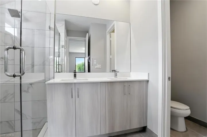 Full bath with a marble finish shower, double vanity, and dark tile patterned floors