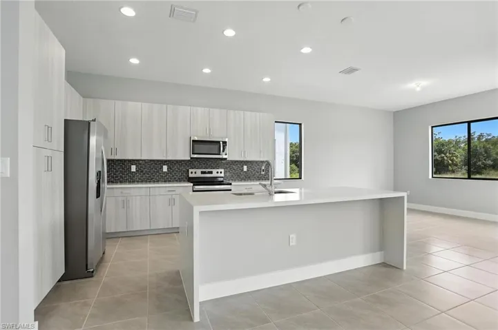 Kitchen featuring light stone counters, light tile patterned flooring, backsplash, appliances with stainless steel finishes, and an island with sink