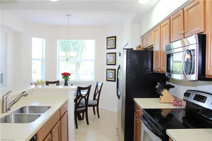 Kitchen with stainless steel appliances, light countertops, hanging light fixtures, brown cabinetry, and recessed lighting