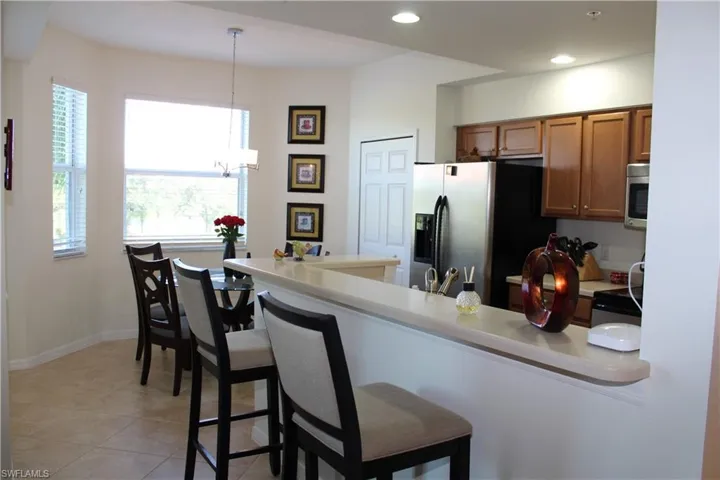 Kitchen with a breakfast bar area, brown cabinets, light countertops, appliances with stainless steel finishes, and hanging light fixtures