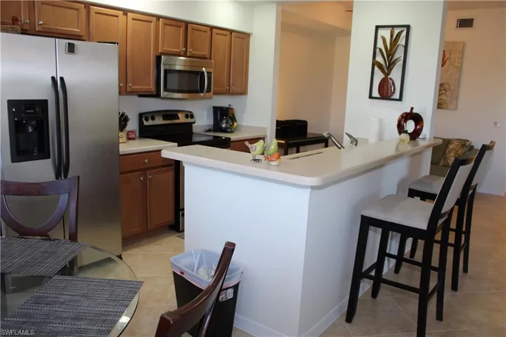 Kitchen featuring stainless steel appliances, brown cabinetry, light countertops, a kitchen breakfast bar, and light tile patterned flooring