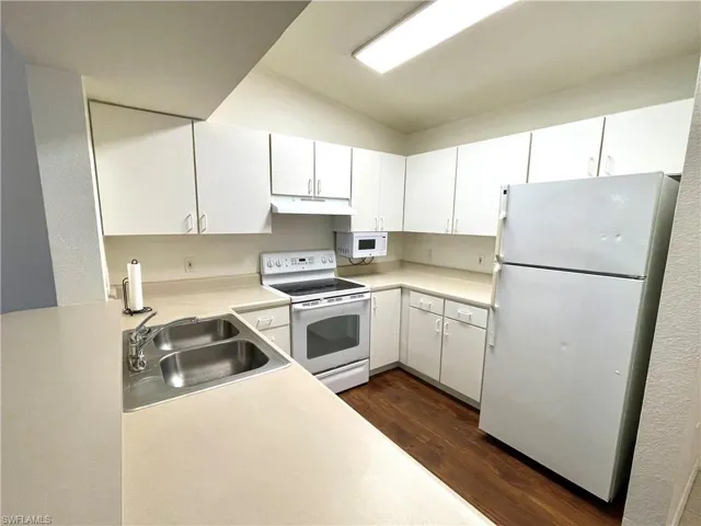 Kitchen with white appliances, dark wood-style flooring, white cabinets, light countertops, and under cabinet range hood