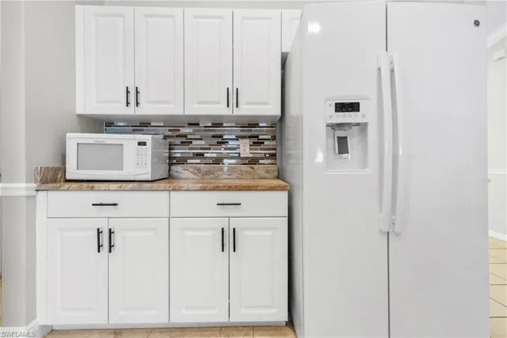 Kitchen with white appliances, backsplash, white cabinetry, light tile patterned floors, and light stone countertops