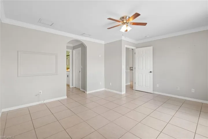Unfurnished room featuring arched walkways, crown molding, a ceiling fan, and light tile patterned floors