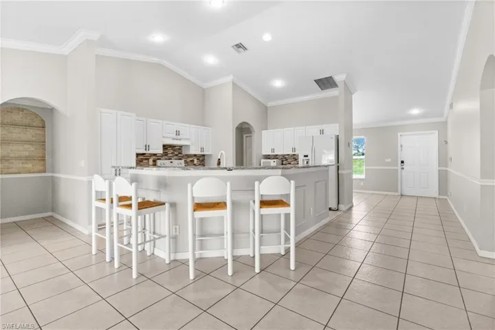 Kitchen featuring a breakfast bar, light tile patterned floors, white cabinetry, backsplash, and arched walkways