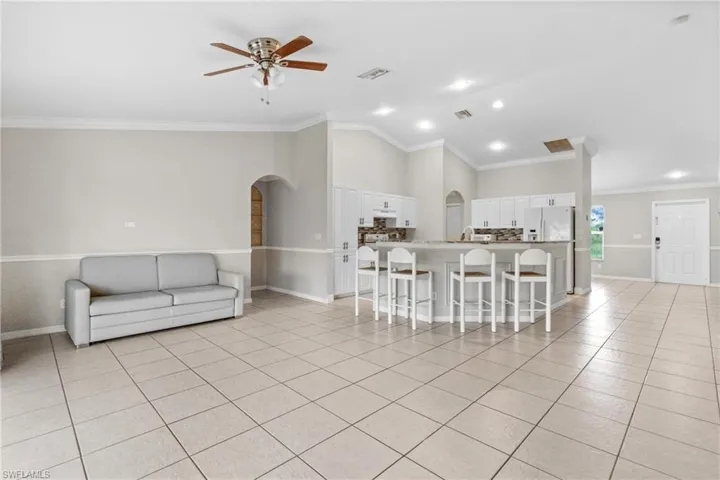 Kitchen with open floor plan, arched walkways, a breakfast bar, white cabinets, and ceiling fan