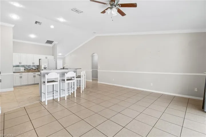 Kitchen featuring ceiling fan, a breakfast bar area, ornamental molding, white cabinets, and tasteful backsplash