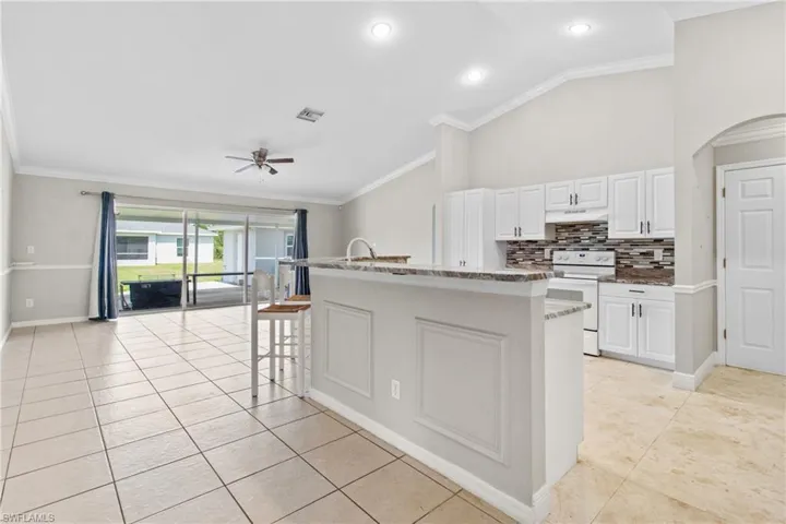 Kitchen featuring white electric stove, vaulted ceiling, light tile patterned flooring, a ceiling fan, and ornamental molding