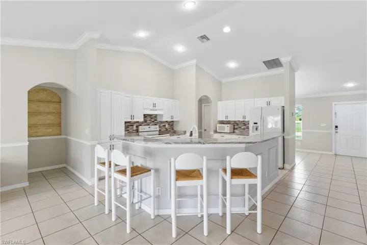 Kitchen with a breakfast bar area, arched walkways, light tile patterned floors, light stone counters, and crown molding