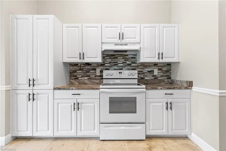 Kitchen featuring white range with electric cooktop, tasteful backsplash, under cabinet range hood, and white cabinetry
